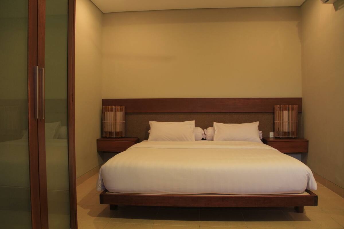 A hotel room with a large bed, wooden headboard, two bedside tables, and a bamboo basket on one table.
