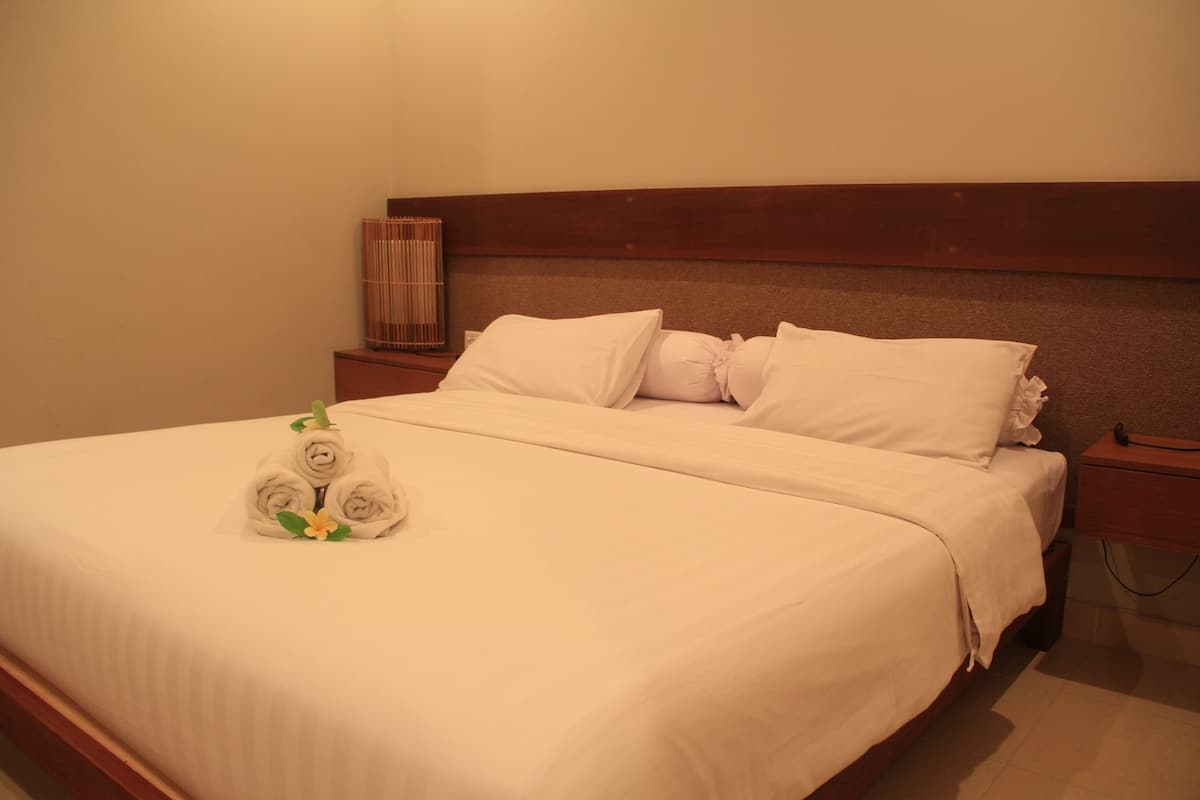 A neatly made bed with white linens, a decorative towel arrangement with flowers, and a wooden headboard.