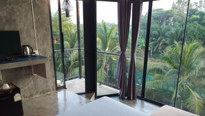 A hotel room with a large window, a bed, a TV, and a minibar. - Plern Salaya Resort (Phutthamonthon)