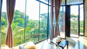 A room with large windows, a sofa, and a small table with a decorative item. - Plern Salaya Resort (Phutthamonthon)