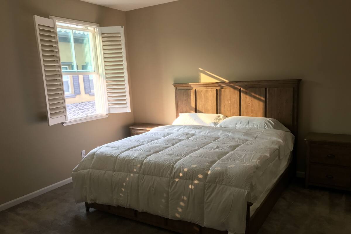 A bedroom with a bed, a nightstand, a wooden headboard, and a window with open shutters.