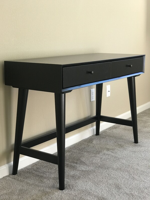 A black desk with two drawers against a beige wall, with a power outlet visible on the wall. - Shared Private Home at Santana Row (San Jose)