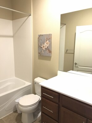 A bathroom with a bathtub, toilet, vanity with drawers, and a mirror. - Shared Private Home at Santana Row (San Jose)