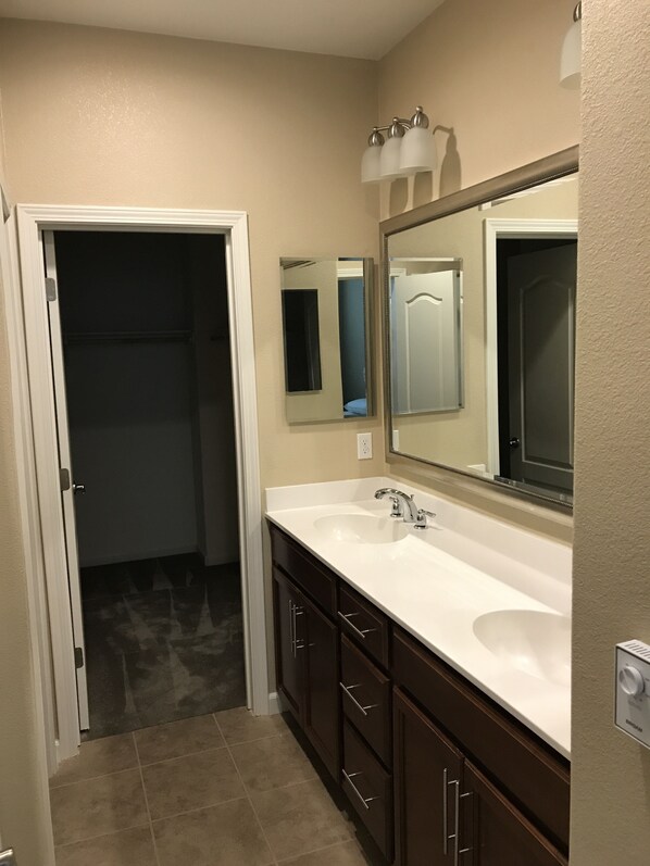 A bathroom with a white sink, dark wooden cabinets, a large mirror, and a door leading to a closet. - Shared Private Home at Santana Row (San Jose)