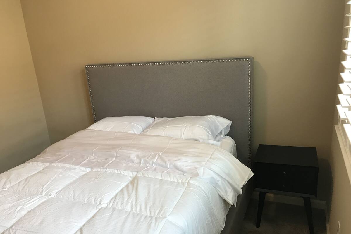 A neatly made bed with a grey headboard and white bedding in a room with beige walls.
