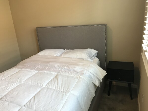 A neatly made bed with a grey headboard and white bedding in a room with beige walls. - Shared Private Home at Santana Row (San Jose)