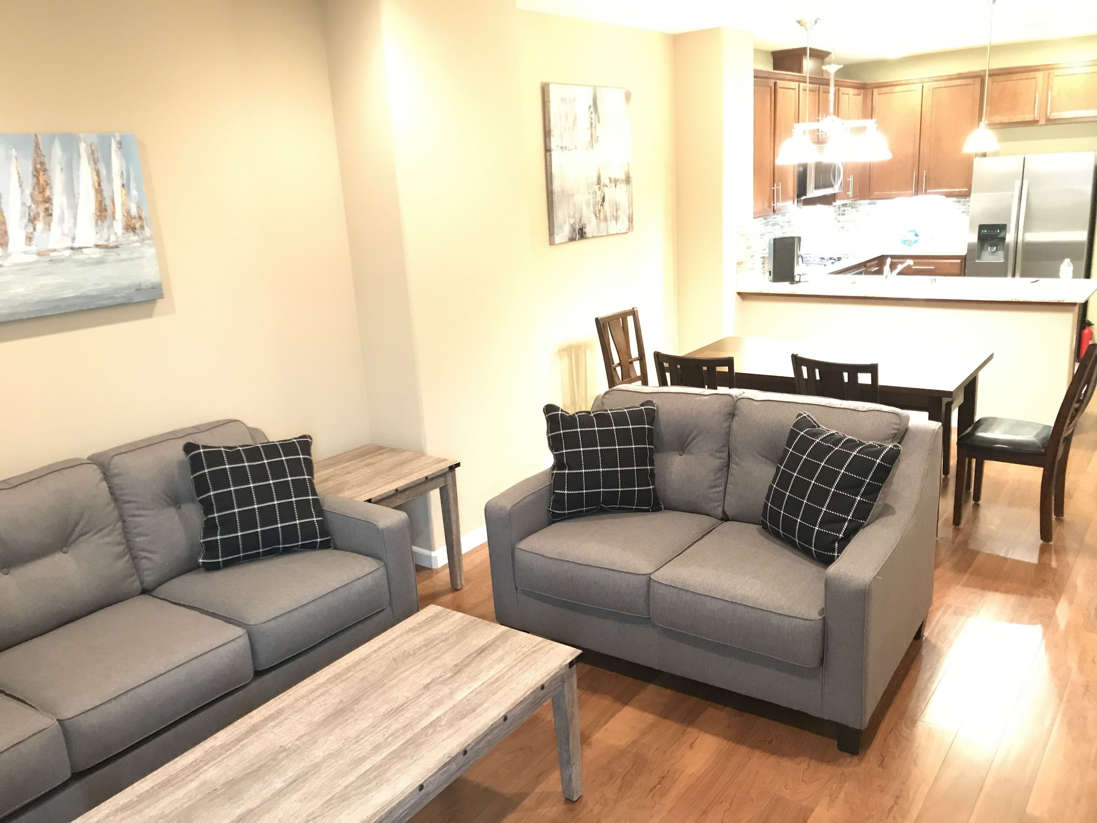 Una sala de estar con un sofá gris, una mesa de centro de madera y una zona de comedor con una mesa y sillas de madera.