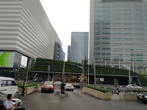 Een moderne, stedelijke straat met hoge gebouwen, een groen ingericht gebied en geparkeerde auto's langs de weg.