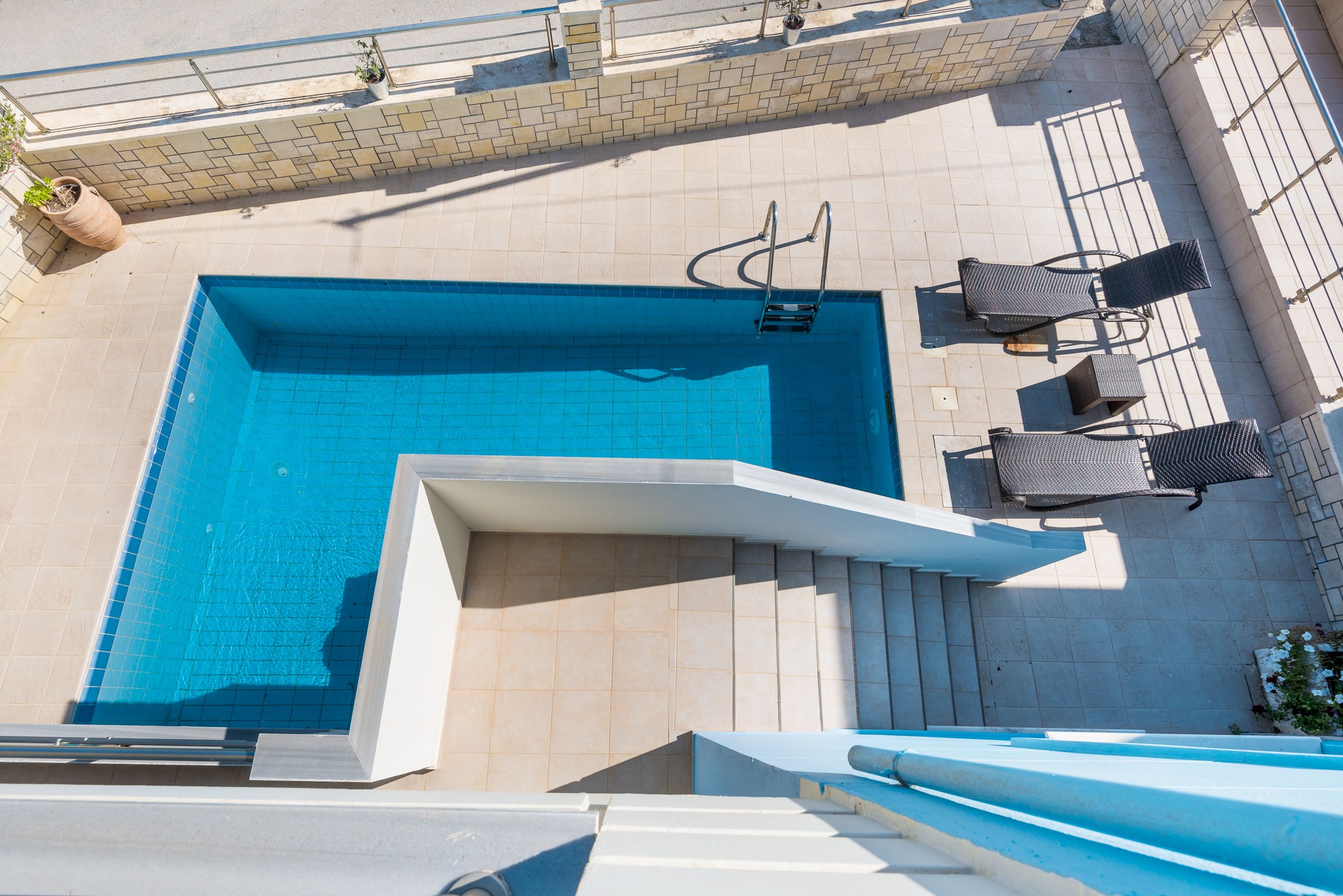 Une piscine rectangulaire avec un escalier en métal, entourée de carreaux de couleur beige.