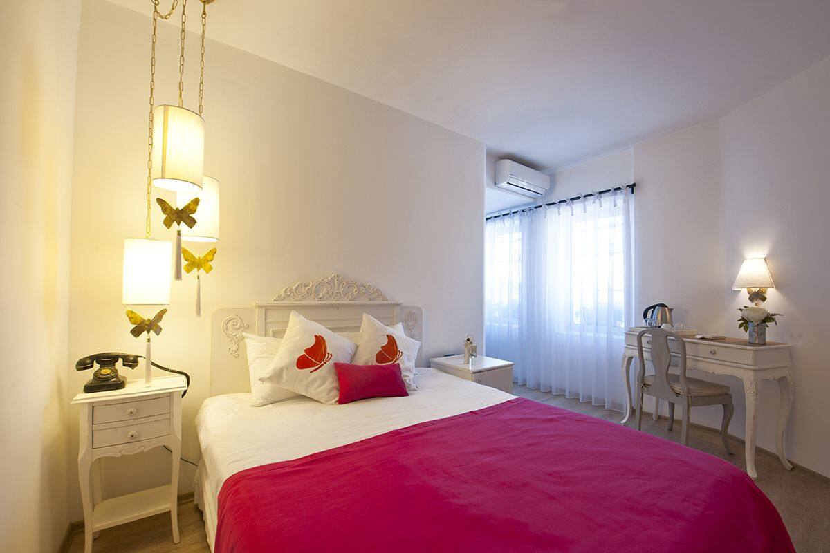 A hotel room with a bed, bedside tables, a desk, and an air conditioning unit.