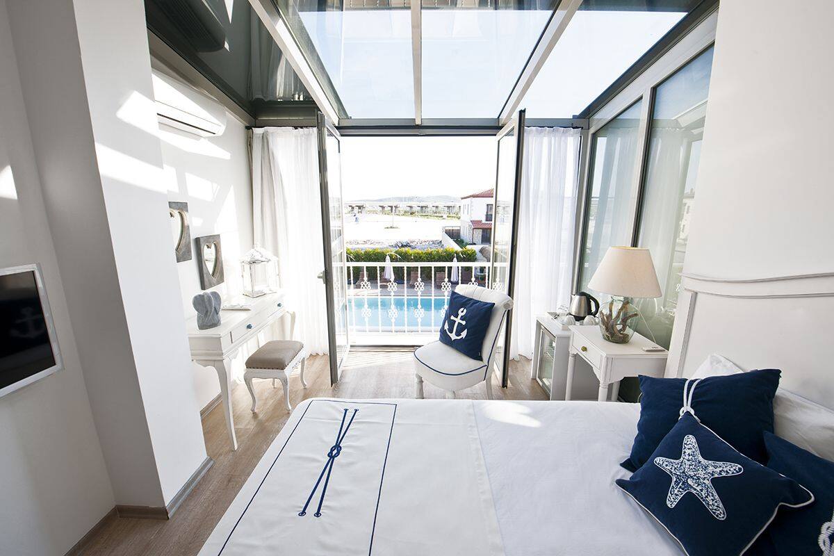 A hotel room with a balcony, a bed with nautical-themed bedding, a desk, and a chair.