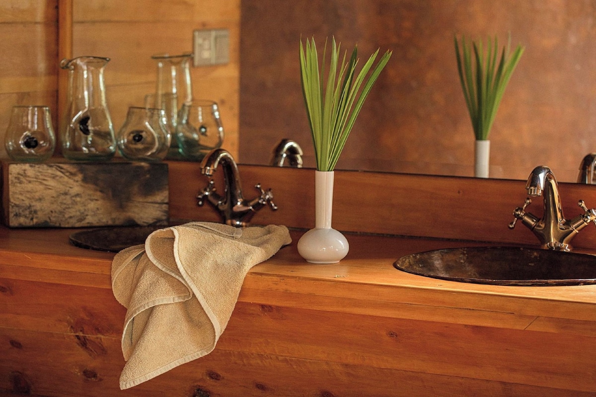 A wooden countertop with a sink, a towel, and a vase with green plants.