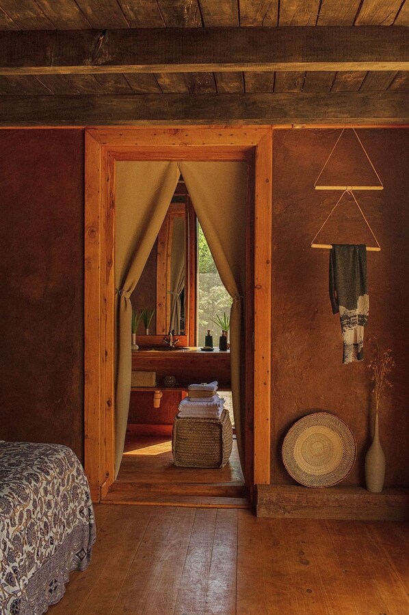 A wooden room with a bed, a vanity with a mirror, and a small window with curtains.