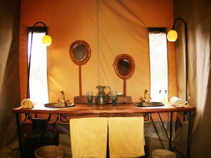 A rustic bathroom with a wooden vanity, two mirrors, a sink, and a towel rack. - Olengoti Safari Camp - East Africa Camps (Maasai Mara)