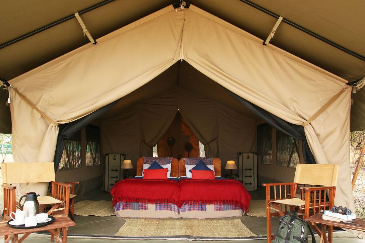 A tented accommodation with a bed, two chairs, a table, and a coffee setup.