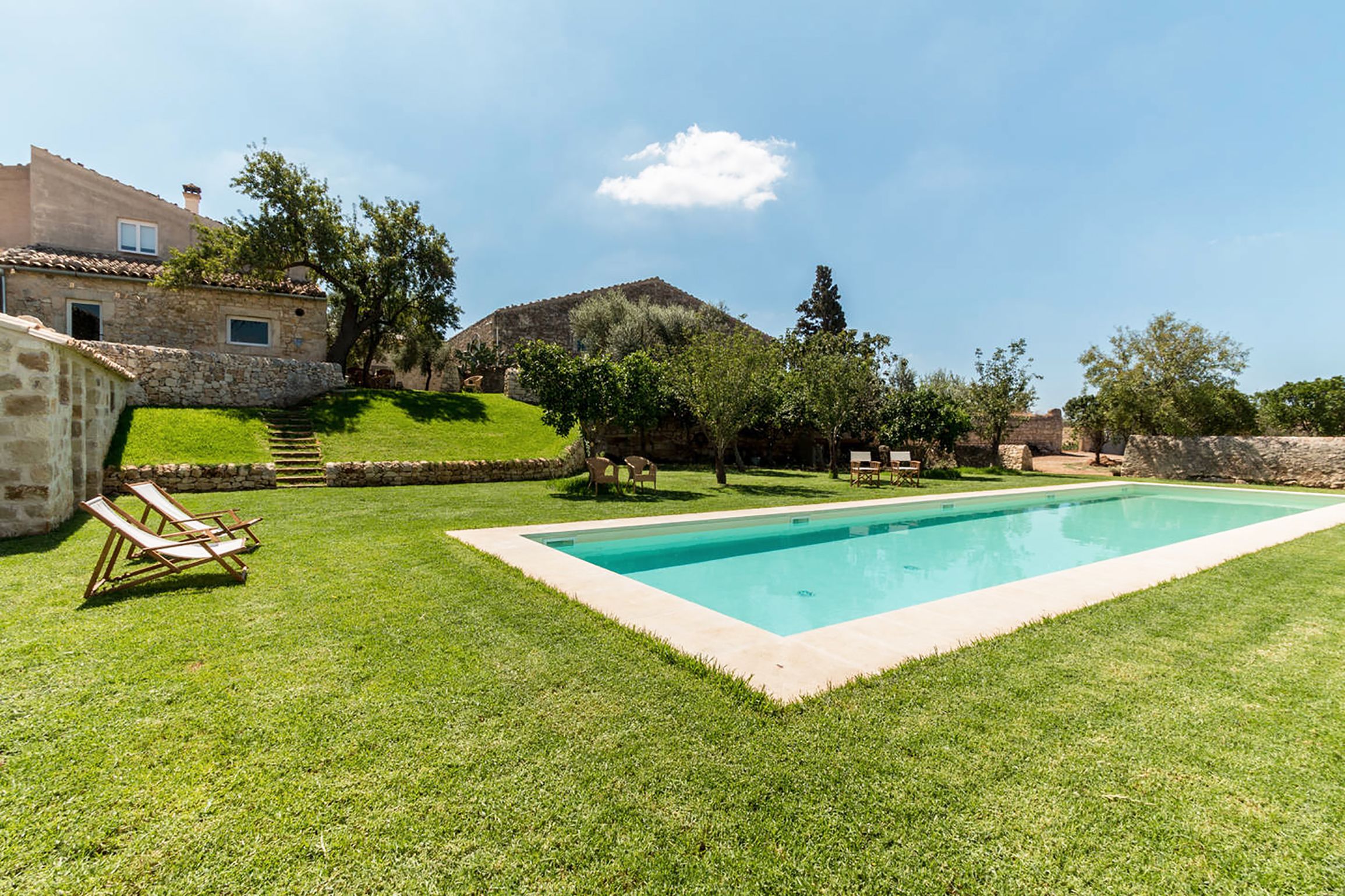 Una piscina rodeada por un césped cuidado, muros de piedra y un edificio de piedra.