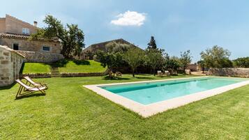 Una piscina rodeada por un césped cuidado, muros de piedra y un edificio de piedra.