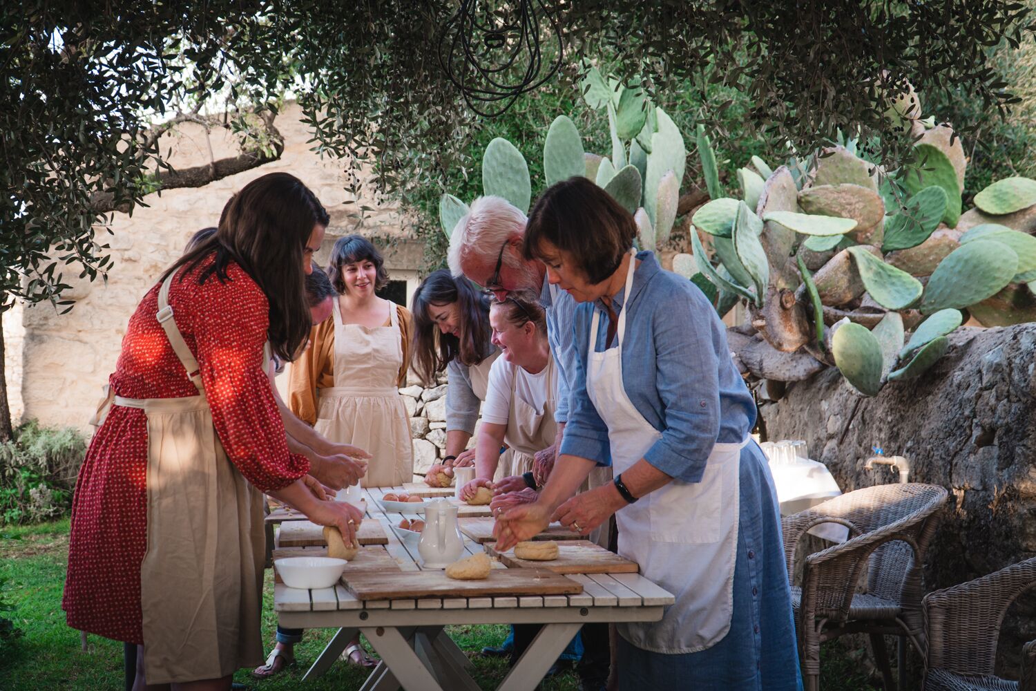 A group of people outdoors, preparing food at a wooden table.
