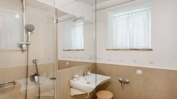 A modern bathroom with a glass shower enclosure, a sink with a mirror, and a window with curtains.