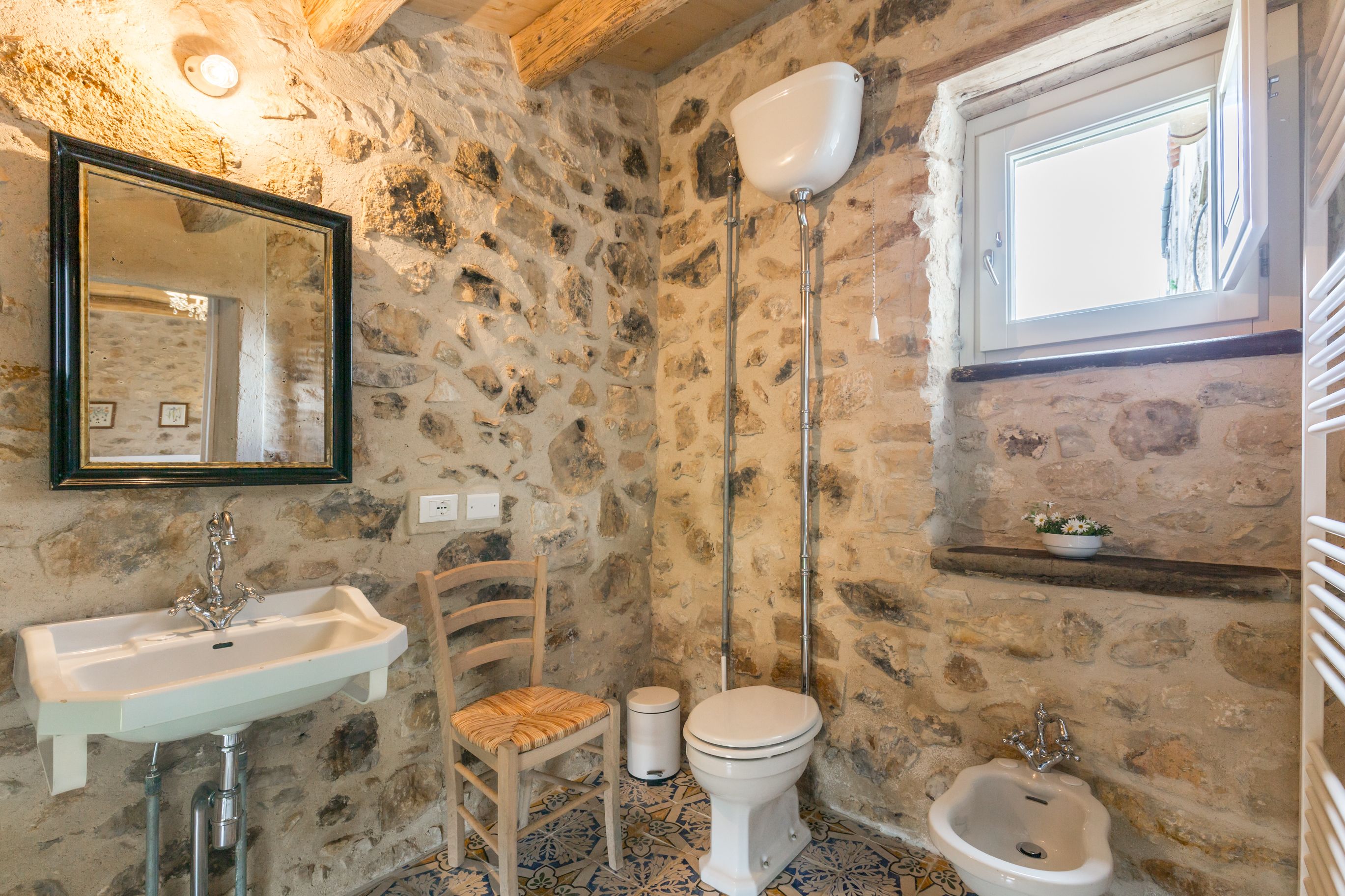 A stone-walled bathroom with a sink, toilet, bidet, and a mirror.