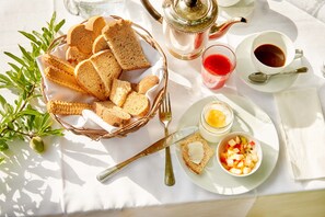 Una escena de desayuno con pan, mermelada, mantequilla y café sobre una mesa.