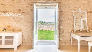 Una habitación con pared de piedra, un tocador blanco con espejo y una puerta que da a otra pared de piedra y una zona con césped.