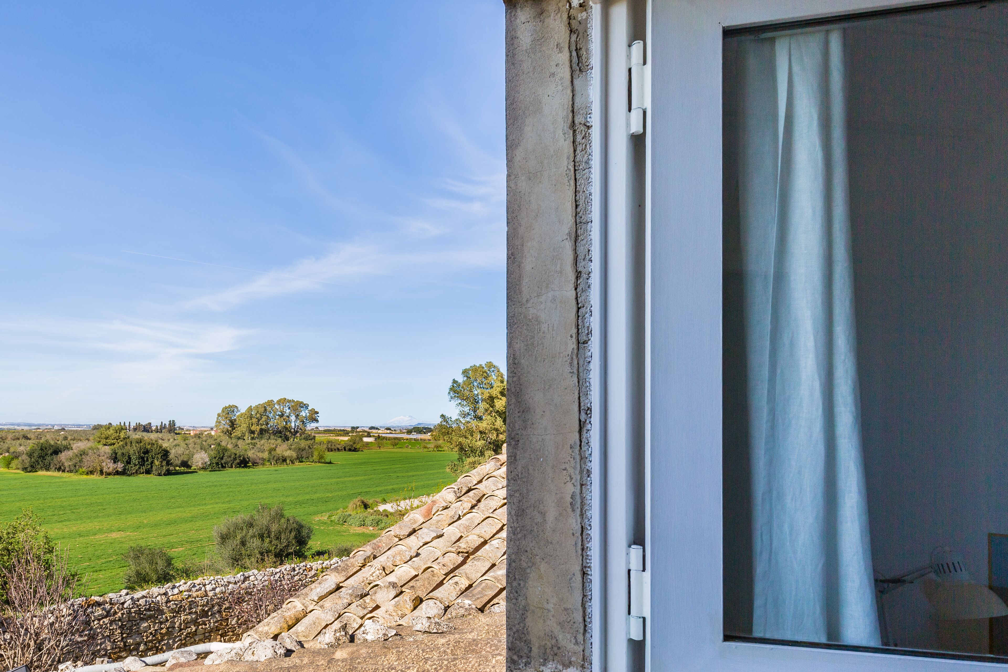 Ein Zimmer mit großem Fenster, das auf eine Steinmauer und ein grünes Feld blickt.