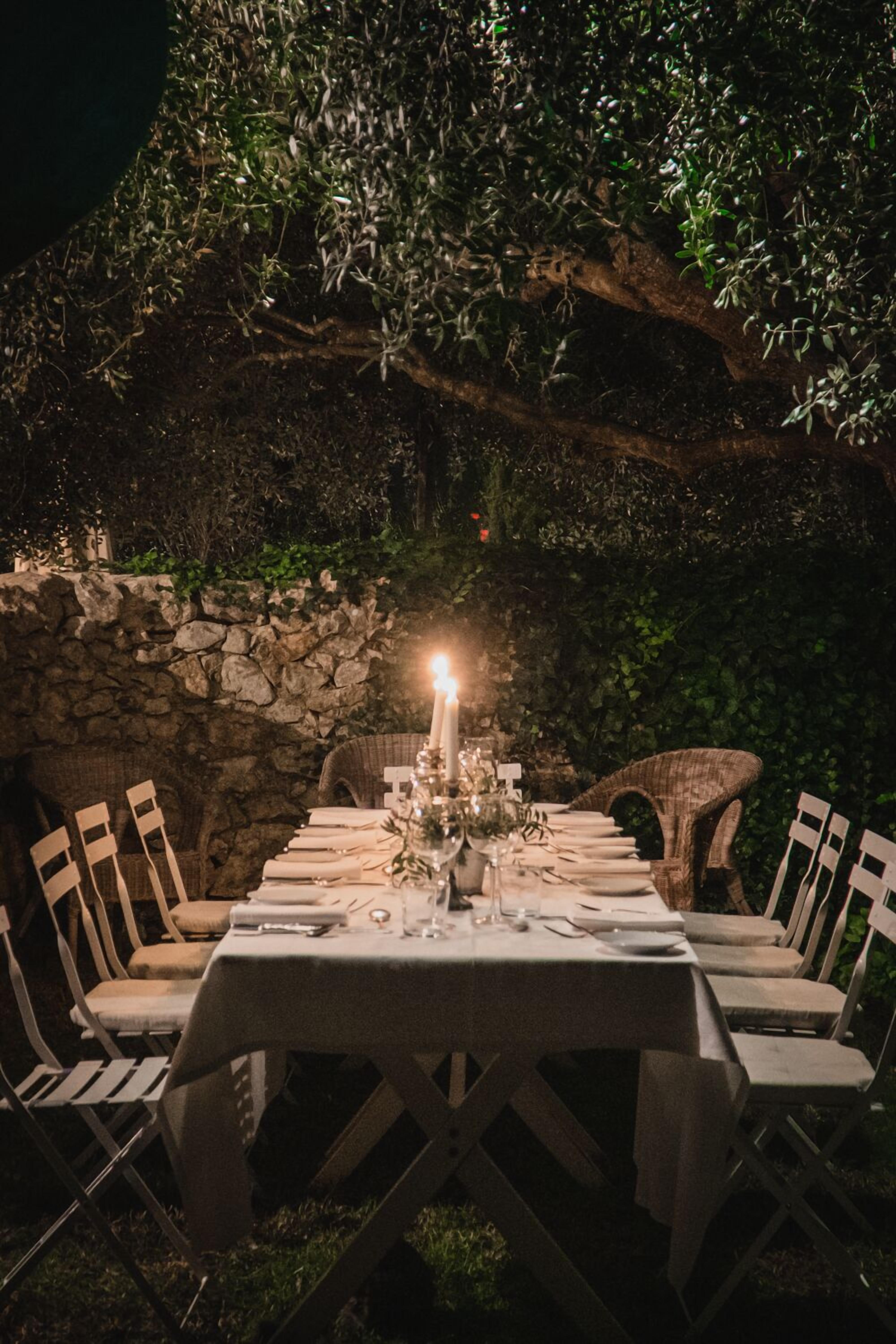 An outdoor dining area with a stone wall backdrop, a table set for four, and chairs.