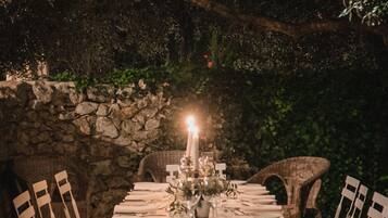 An outdoor dining area with a stone wall backdrop, a table set for four, and chairs.
