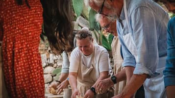 Un grupo de personas participa en una actividad culinaria al aire libre, con un muro de piedra y vegetación de fondo.