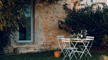 An outdoor dining area with a stone wall, a window, and a table set with chairs and a basket.