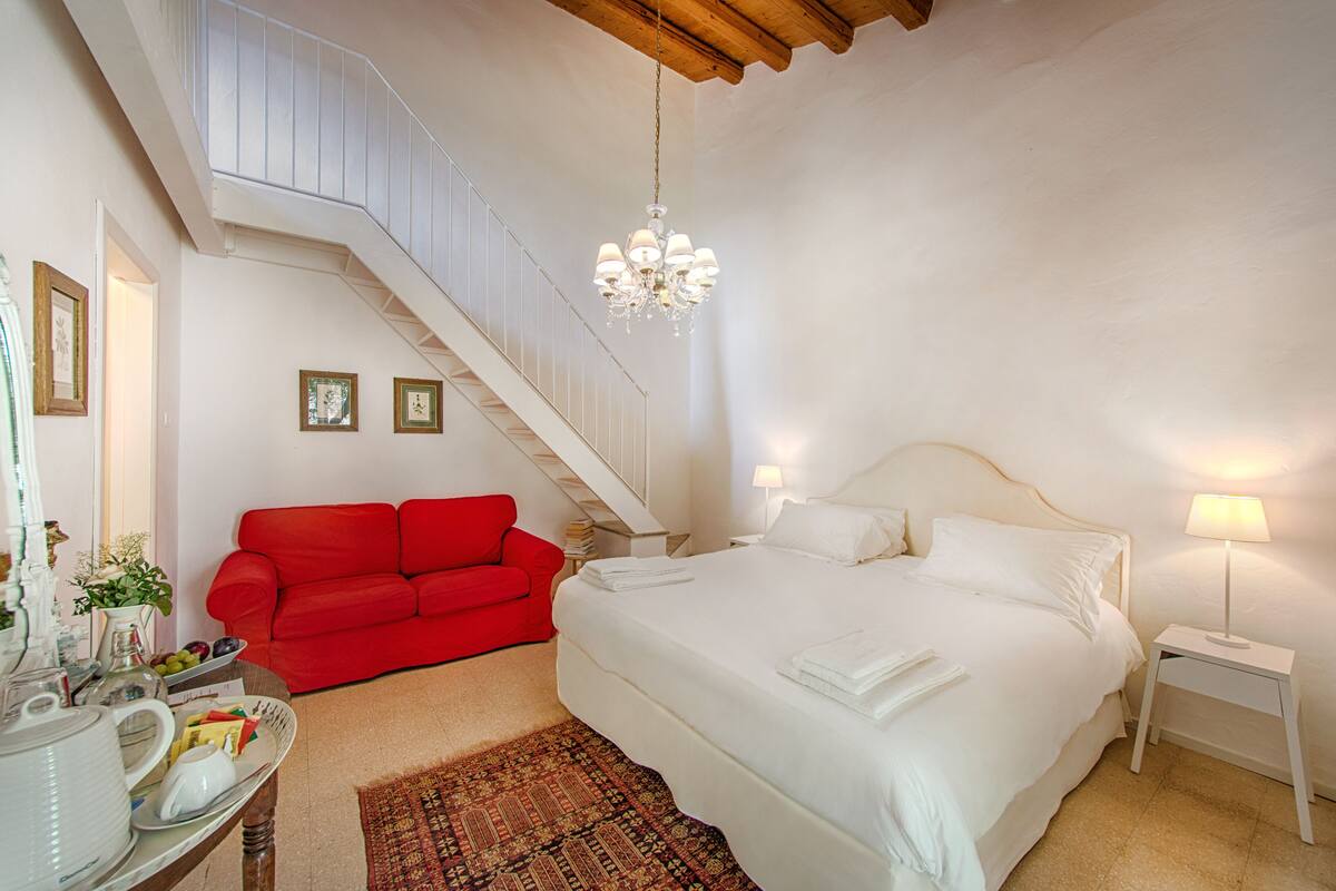 A bedroom with a large bed, a red sofa, a staircase, and a chandelier.