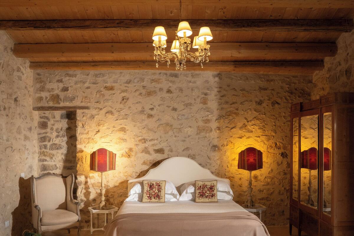 A room with a bed, two lamps, a chair, and a mirror.