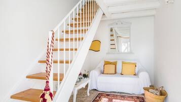 Una escalera con barandillas blancas y escalones de madera conduce a un dormitorio con una cama blanca, almohadas amarillas y una alfombra estampada.