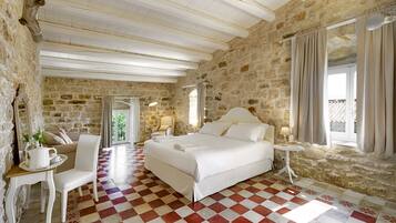 Une chambre spacieuse avec un grand lit, une chaise, une petite table et un mur en pierre.