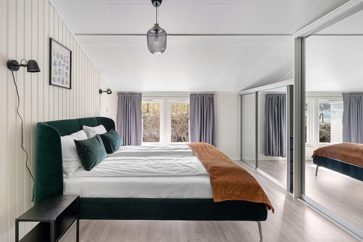 A modern bedroom with a large bed, a bedside table, a hanging light fixture, and a view through a glass door.