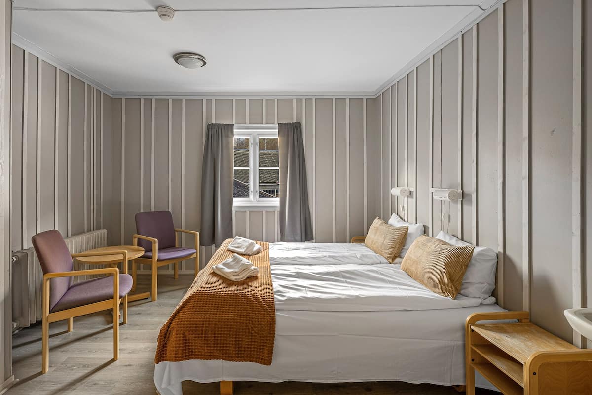 A hotel room with a bed, a chair, a small table, and a window with curtains.