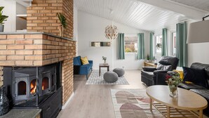 Una sala de estar acogedora con chimenea de ladrillo, un sofá azul, un sillón de cuero y una mesa de centro de madera.