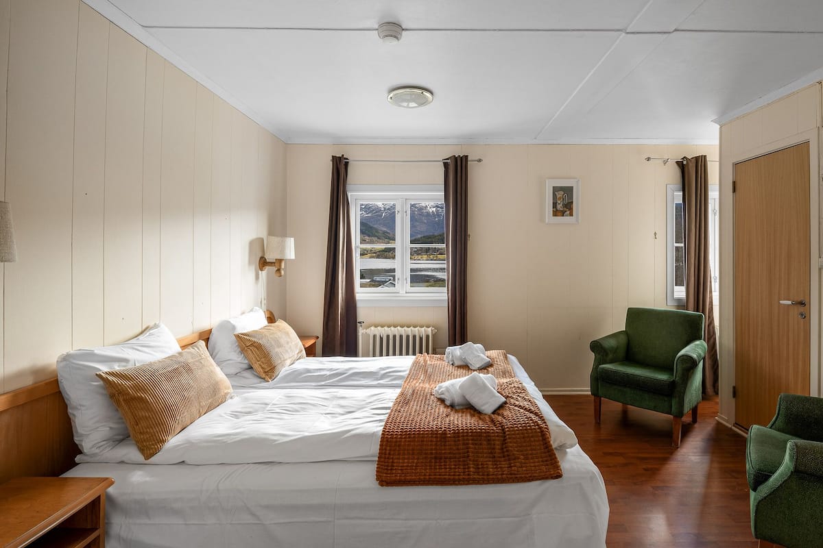 A hotel room with a bed, a chair, a radiator, a window with a view, and a door.