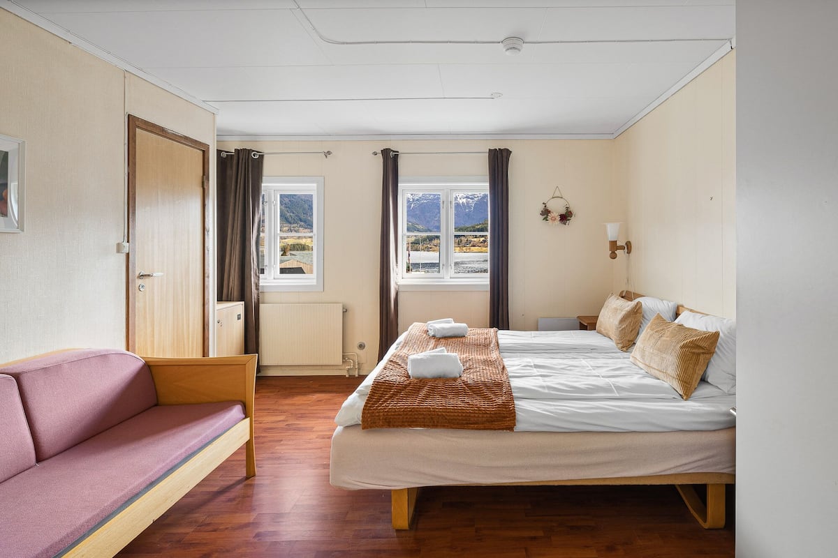 A bedroom with a bed, a sofa, a window with a mountain view, and a radiator.