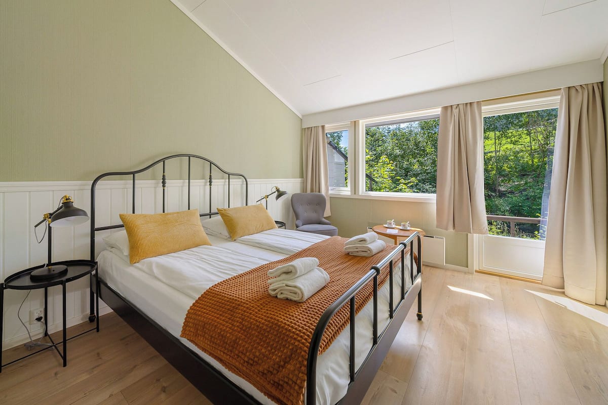 A bedroom with a bed, a chair, a table, and a window with curtains.