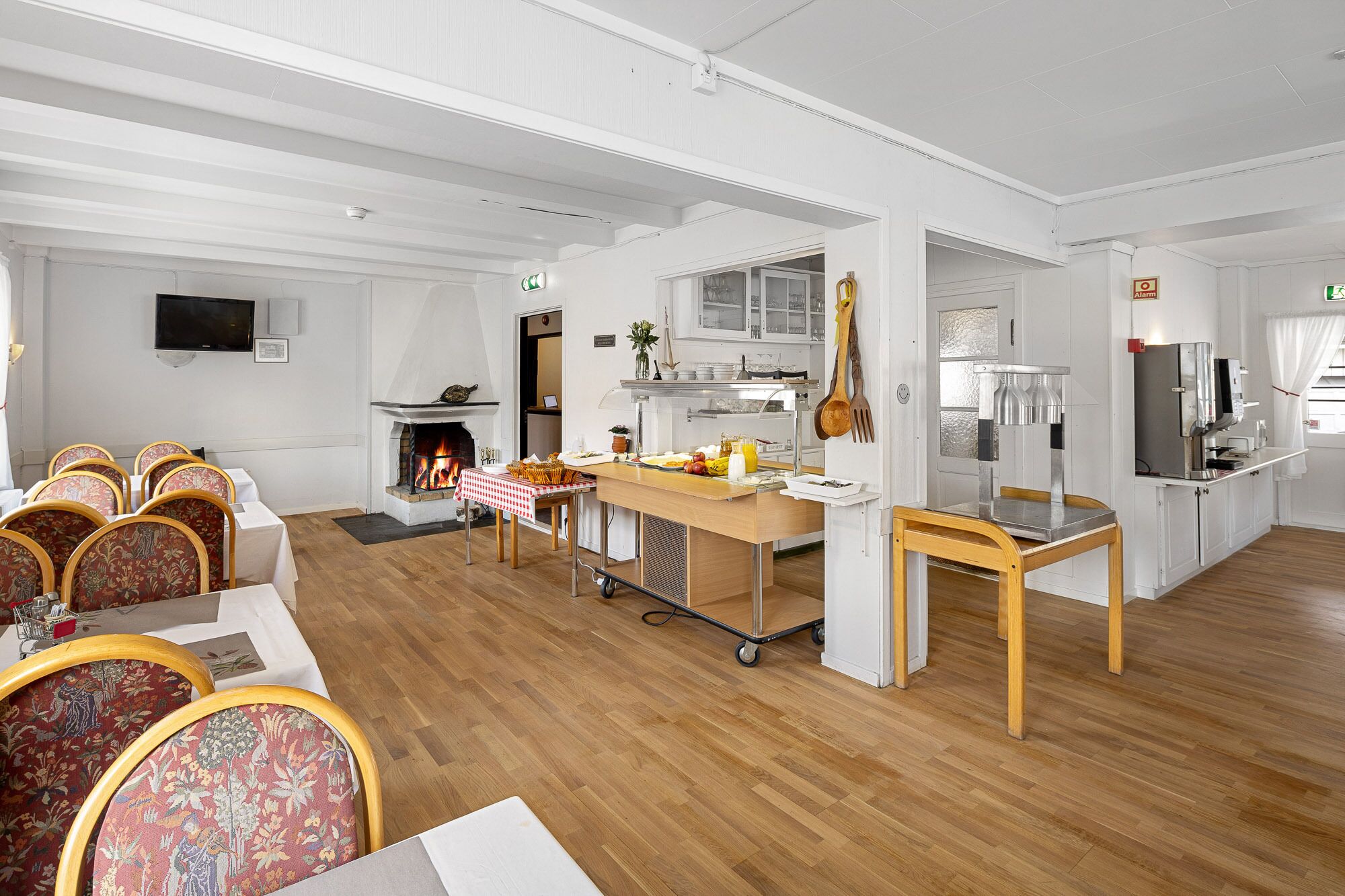 Un'ampia stanza con camino, zona pranzo con sedie floreali, cucina con elettrodomestici moderni e un'ampia finestra.