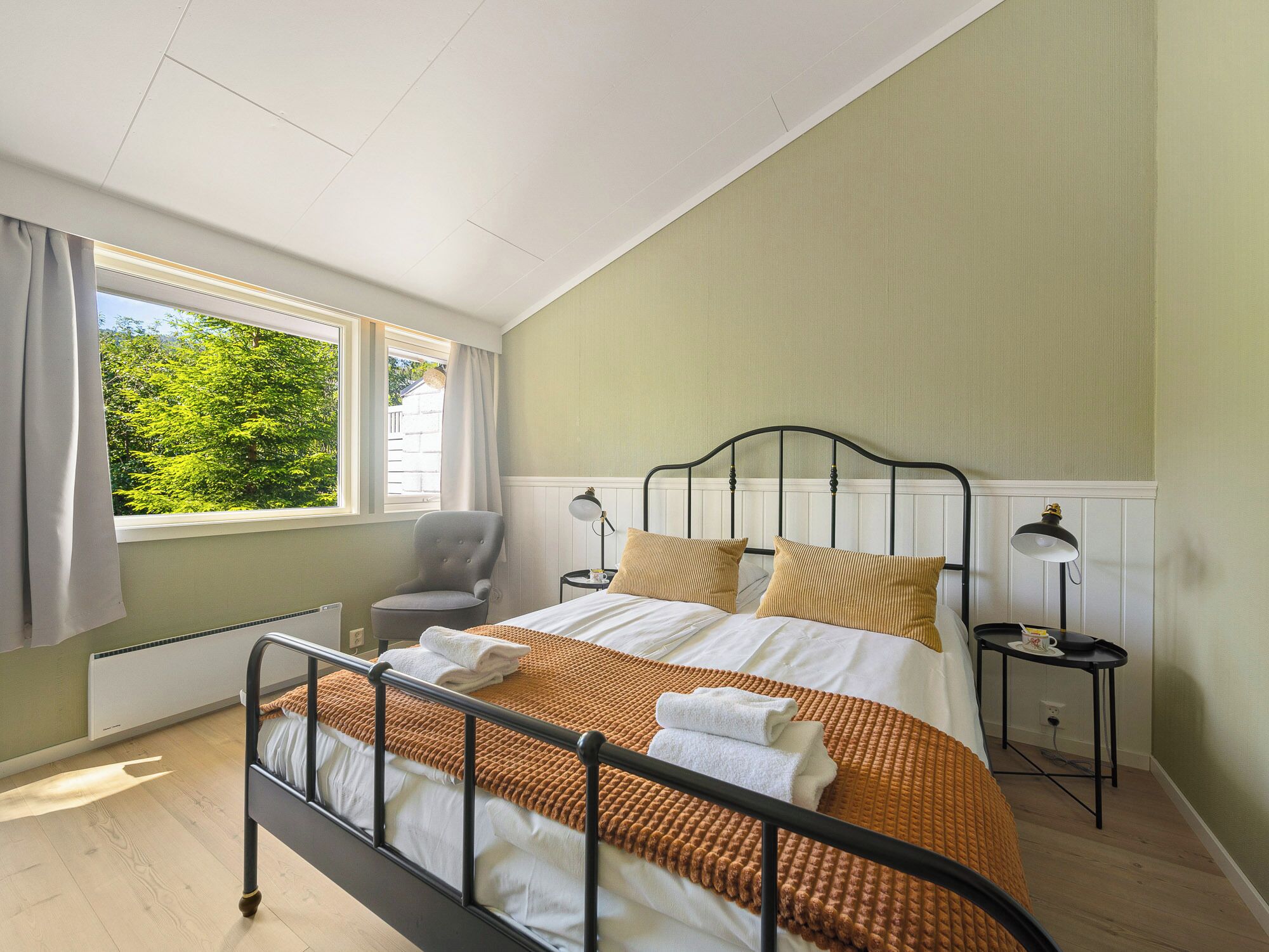 A bedroom with a bed, a chair, a nightstand, and a window with a view of trees.