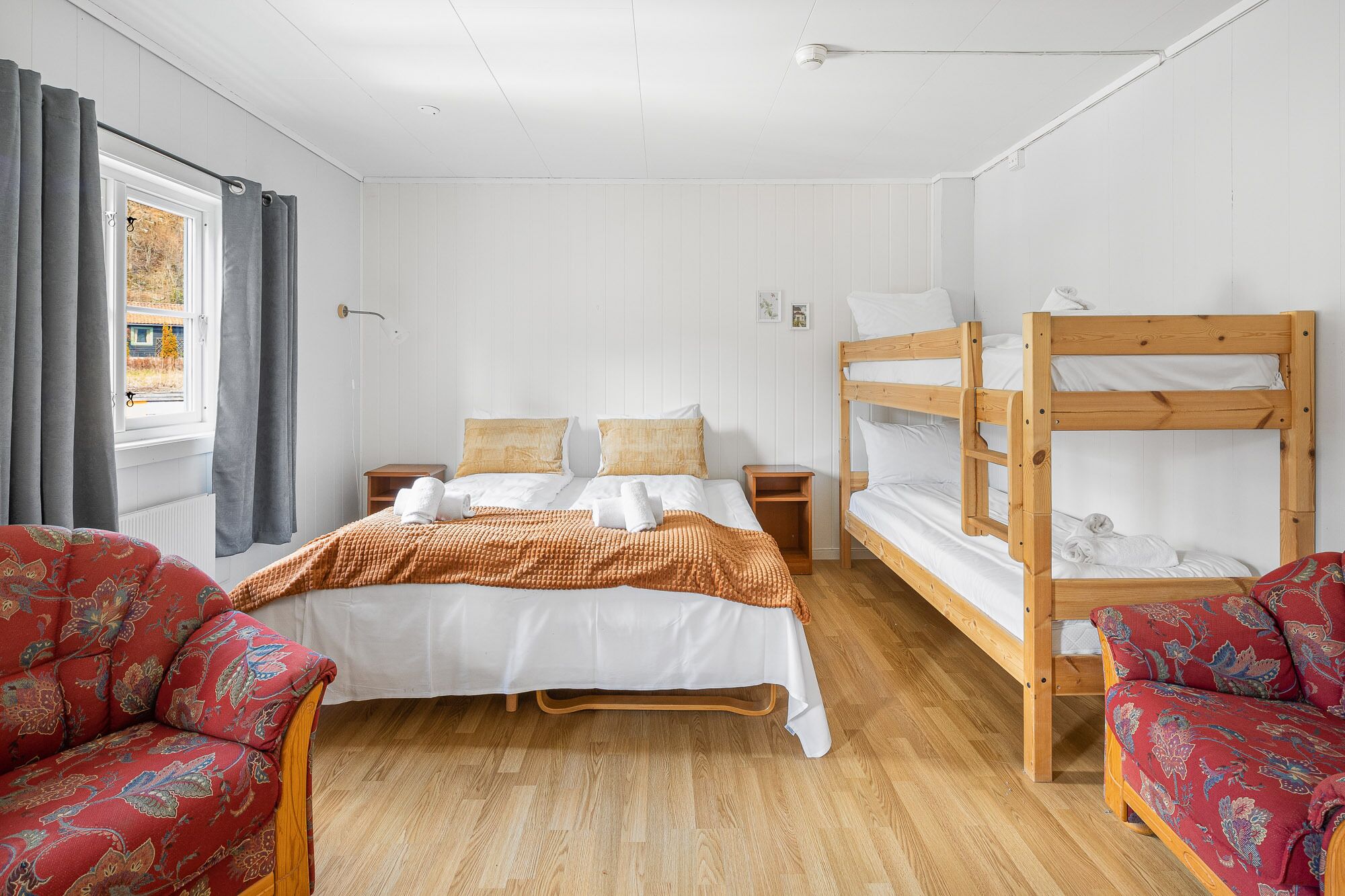 A room with a bunk bed, a single bed, and two armchairs.