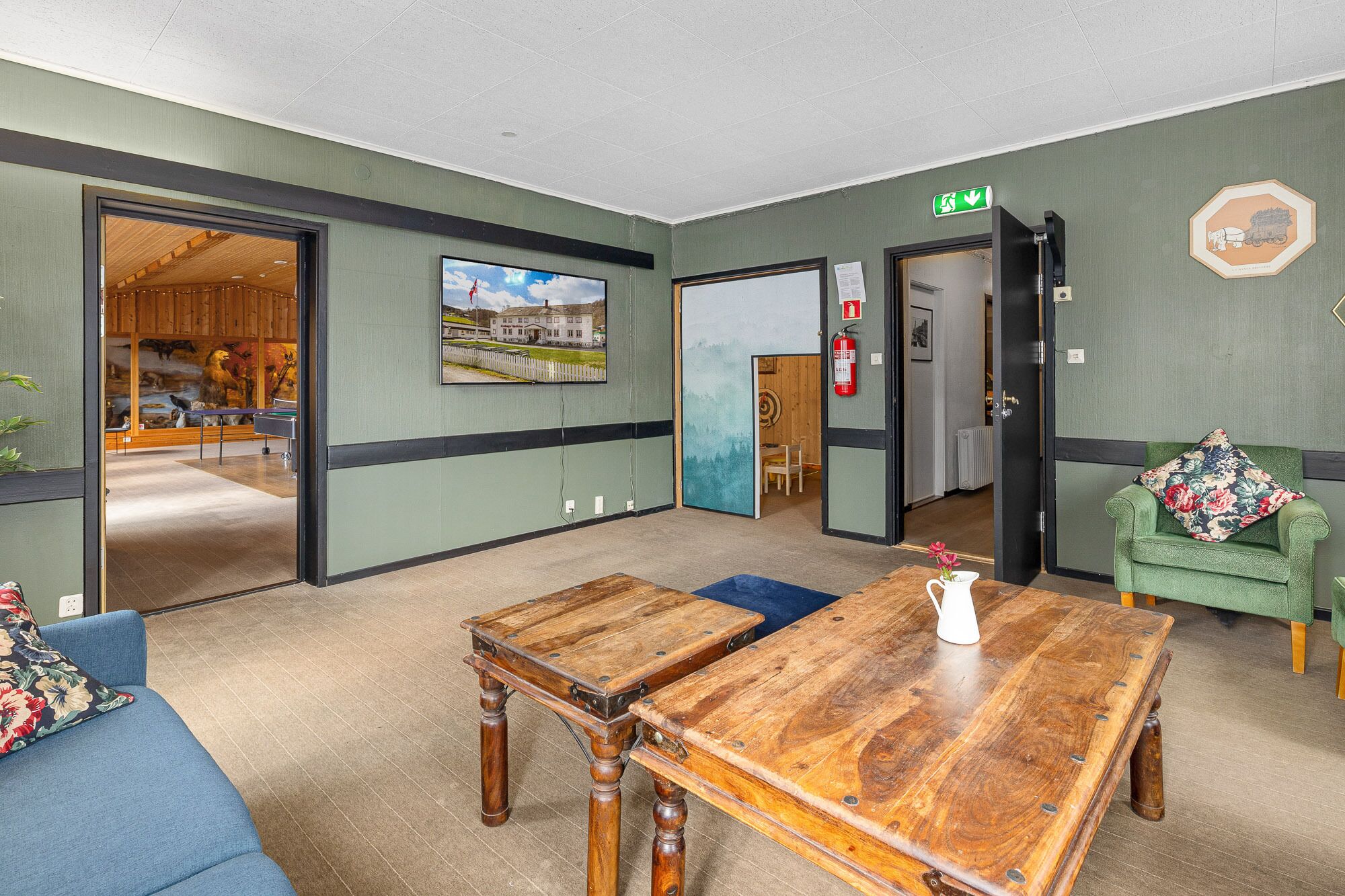A hotel lobby with a wooden coffee table, a green sofa, and a blue couch. There is a door leading to a dining area with a view of a building.