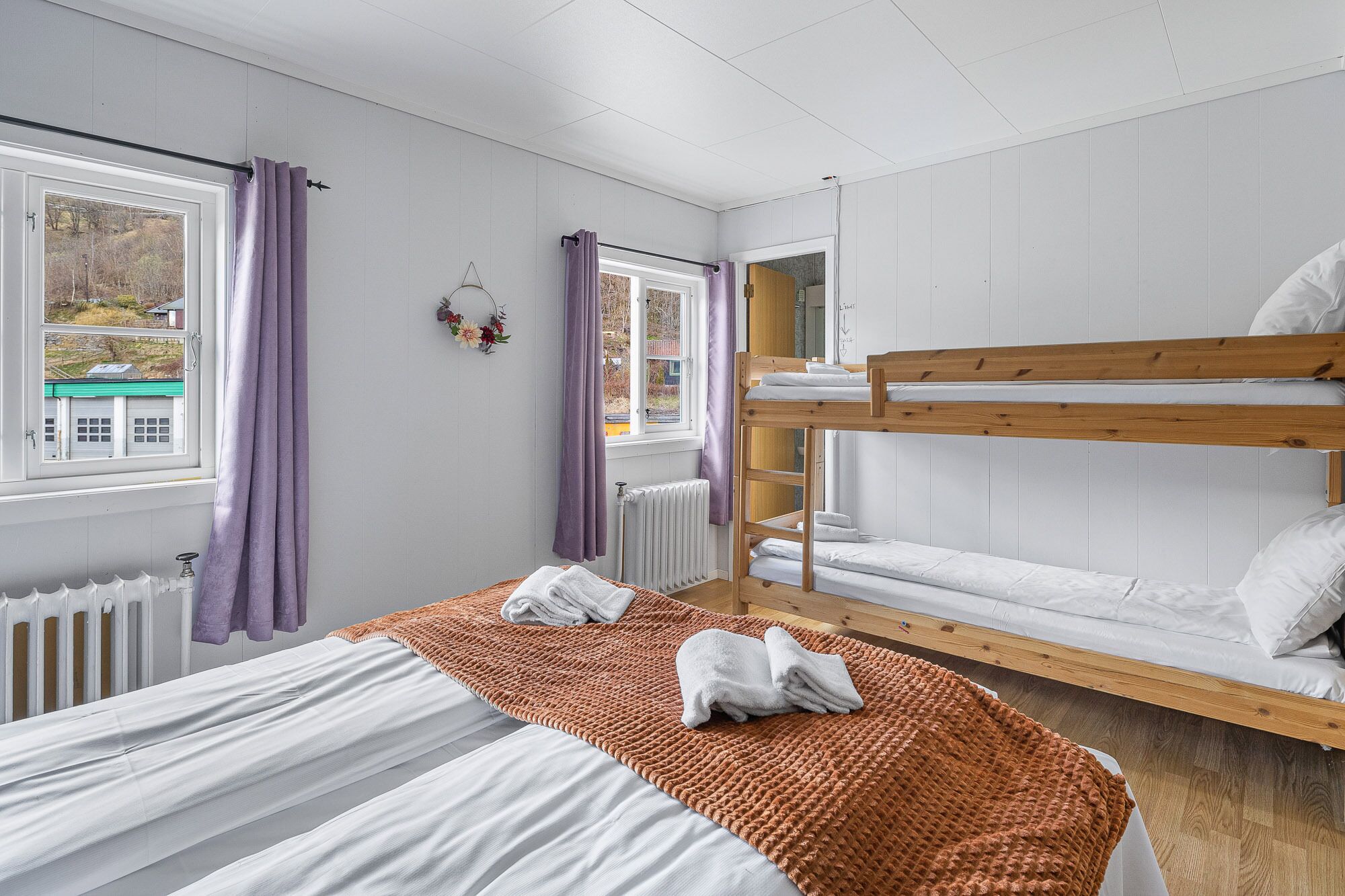 Ein Zimmer mit einem Etagenbett, einem Einzelbett und einem Fenster mit Vorhängen.