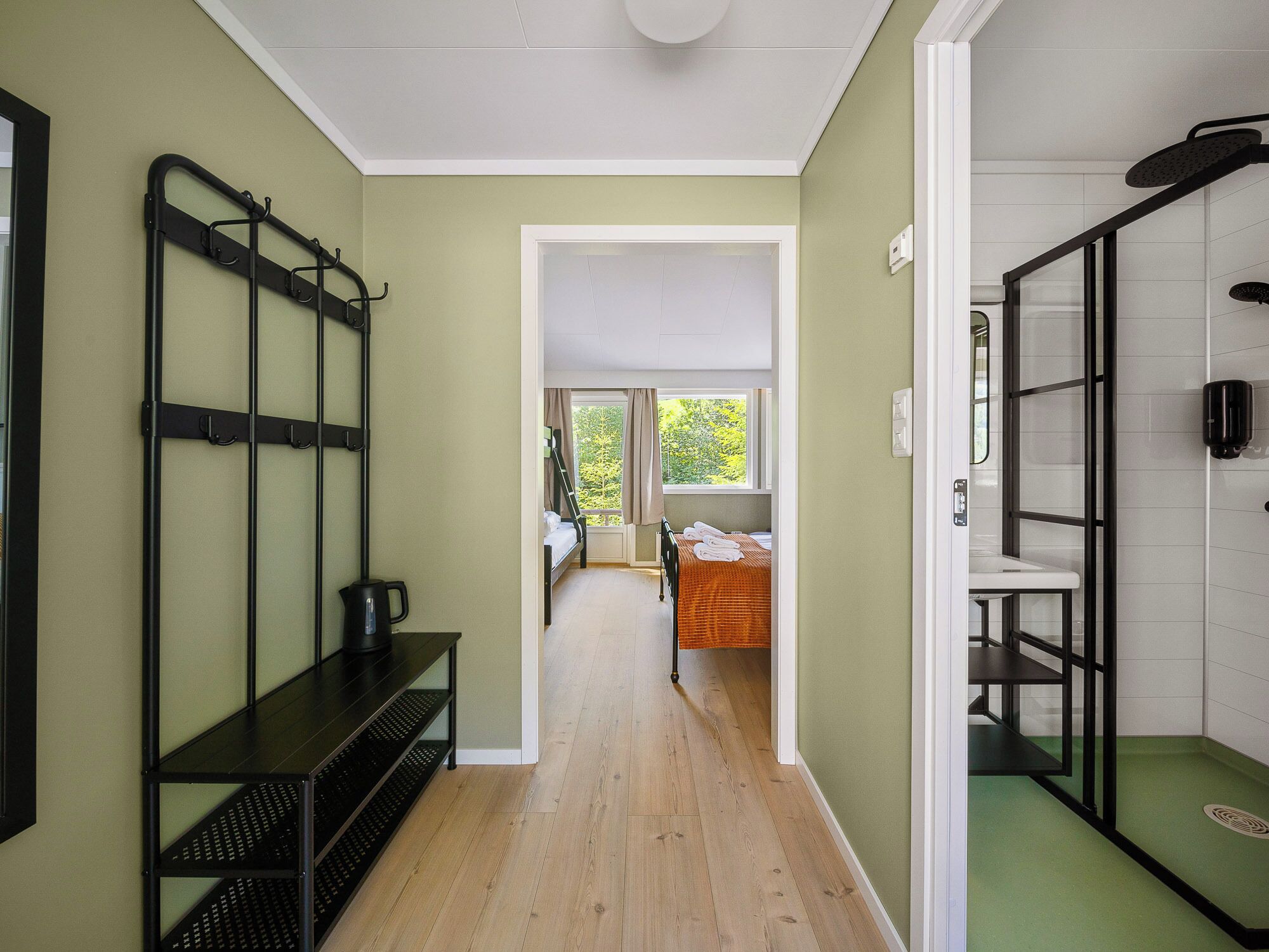 A hallway with a bunk bed, a desk with a kettle, and a shower area.