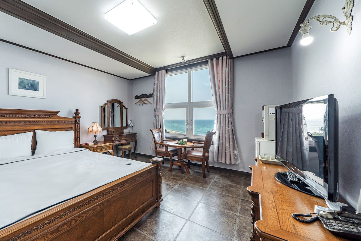 A hotel room with a large bed, a desk with a computer, a TV, and a view of the ocean.