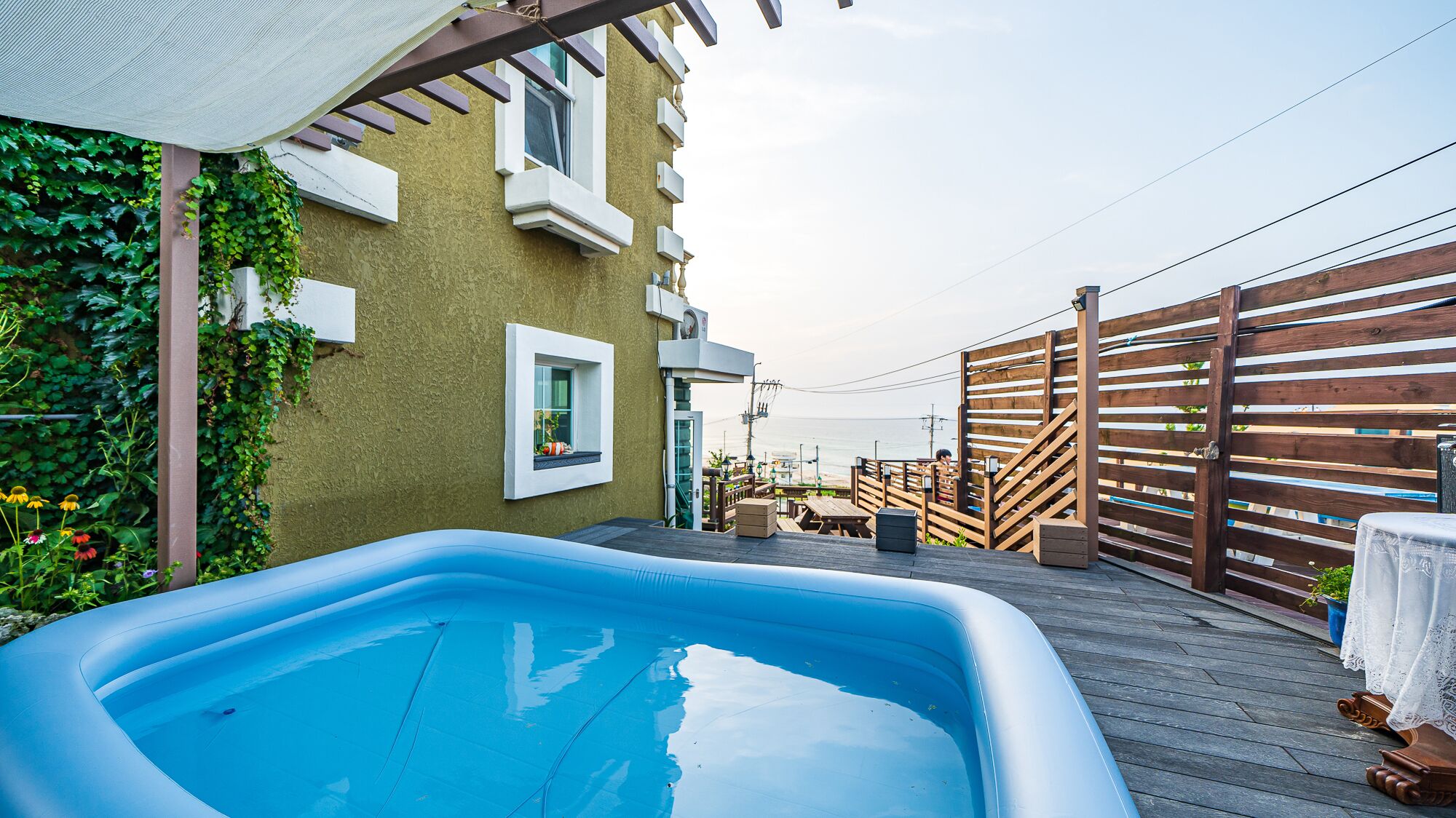 Een buitenzwembad met een houten terras, een pergola en uitzicht op zee.