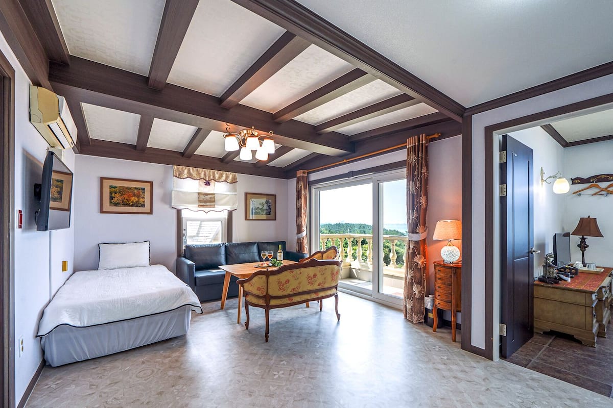 A bedroom with a bed, a desk, a chair, and a balcony with a view.